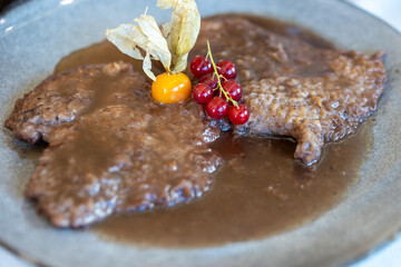 tender veal schnitzel topped with a savory brown gravy, garnished with vibrant physalis and fresh...