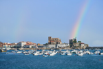 Rainbow over marina de castro urdiales, church of santa maria and lighthouse castle in cantabria, spain