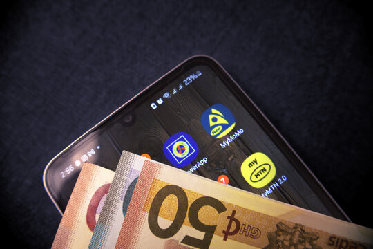 Accra, Ghana - July 7, 2025: Ghana cedis notes on Smartphone with showing MTN  mobile money transfer apps on screen. Top view lay flat. economics concept