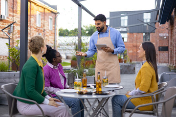 A waiter takes an order from customers at an outdoor restaurant.