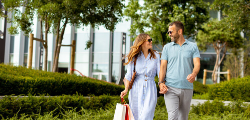 Couple strolls hand in hand through a vibrant outdoor shopping district on a sunny afternoon