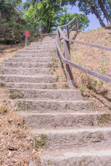 A rustic stone staircase with a wooden railing leading uphill into a wooded area, concept of outdoor exploration, historical sites, nature trails