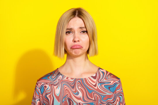 Young woman displaying a pouting expression in a bright yellow setting wearing a colorful patterned top