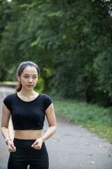 Portrait of a beautiful Asian woman in a black sportswear walking alone on the street after jogging in the morning. The athlete in a black is walking to warm up her body before jogging to get healthy.