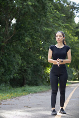 Portrait of a beautiful Asian woman in a black sportswear walking alone on the street after jogging in the morning. The athlete in a black is walking to warm up her body before jogging to get healthy.
