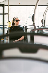 A stylish woman with sunglasses sits calmly on a public bus surrounded by sunlight and empty seats. Perfect for themes of commuting, urban lifestyle, and daily transport routines.