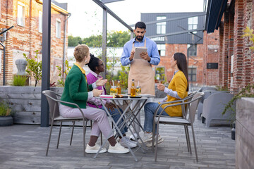 A waiter takes an order from a group of friends sitting at an outdoor cafe table, enjoying drinks...
