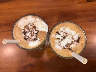 Two glasses of cold coffee with cream and chocolate topping served on wooden table