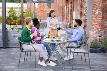A female waiter at an outdoor cafe uses a portable terminal to process a customer's payment.
