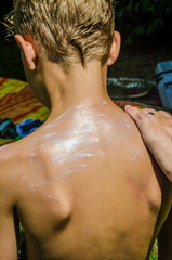 Naklejka premium Applying sunscreen on boys back for sun protection on summer outdoor day. High quality photo