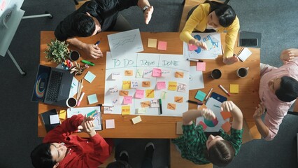 Top down aerial view of smart business team making scrum task board at meeting room. Group of smart people writing at paper and sticky notes for making kanban board and giving high five. Convocation. © InfiniteFlow