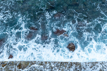 Aerial view captures mesmerizing turquoise and deep blue hues of ocean as waves crash against rocky...