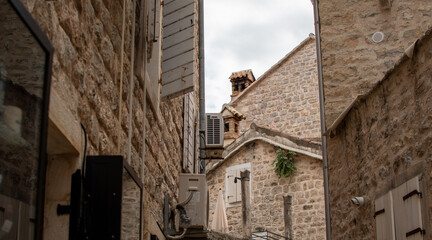 Narrow street or alleyway between two old stone buildings featuring multiple windows with traditional white wooden shutters, some open and some closed under bright sky