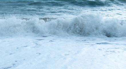 Powerful ocean waves crash and churn, creating significant amount of white sea foam covering the...