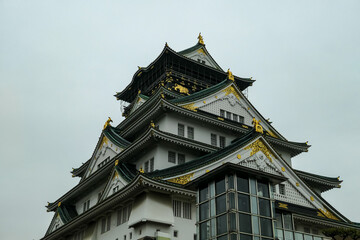 Detailed close-up of the upper tiers of Osaka Castle showcases intricate traditional Japanese...