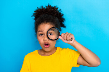 Curious young girl examining objects through a magnifying glass on a vibrant blue background