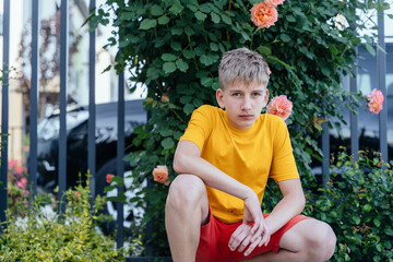Teen boy squatting by rose bush in casual summer outfit