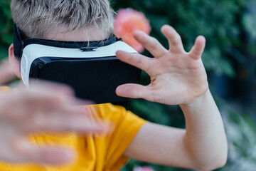 Teen boy using VR headset in blooming garden, hands raised