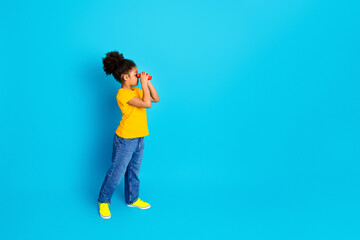 Young girl in vibrant casual style exploring with binoculars against solid azure background.