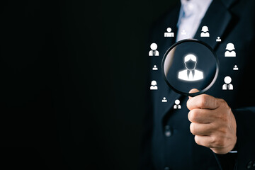 businessman holds a magnifying glass focus on a glowing user icon surrounded by people symbols,...