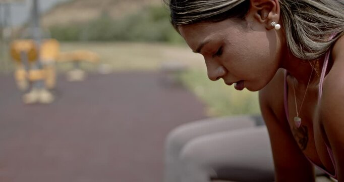 Two diverse female friends take a break during an outdoor workout, catching their breath and wiping away sweat on a hot summer day.