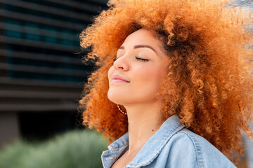 Closeup headshot portrait of young ginger african amerian woman with curly afro hair breathing with...