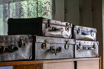 Vintage, worn-out suitcases stacked on a wooden dresser in a room with a lace curtain, evoking a nostalgic retro atmosphere.