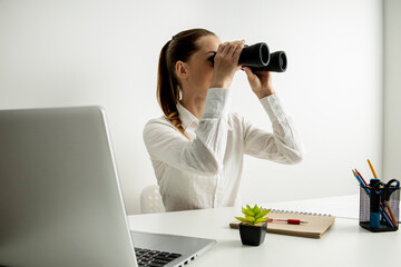 Young woman looking through binoculars sitting in the office at the workplace