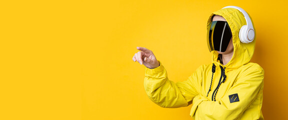 Young woman in cyberpunk glasses with headphones clicks on a virtual screen on a yellow background