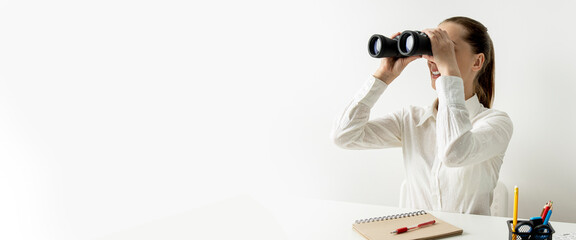 Young smiling woman looking through binoculars while sitting at the workplace. Banner