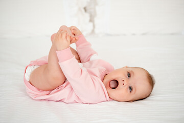 A baby girl plays with her legs lying on her back, a cute and smiling little child in a pink...