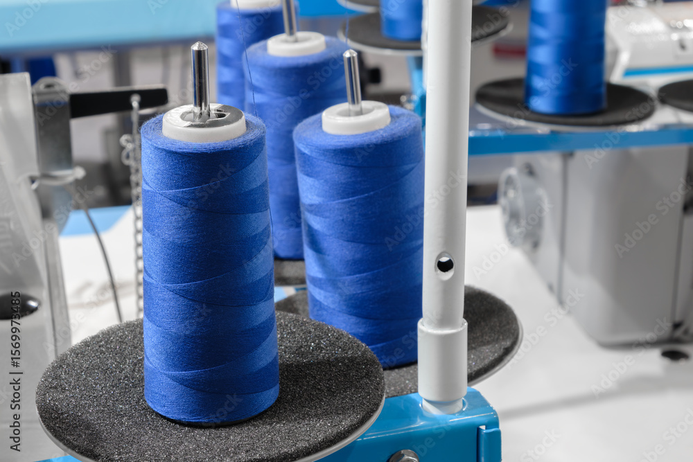 Poster blue spool of thread is on a machine. there are four spools of thread on the machine