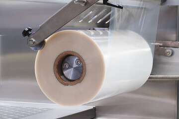 A machine with a roll of polyethylene plastic wrapping film on it. The machine is in a factory....