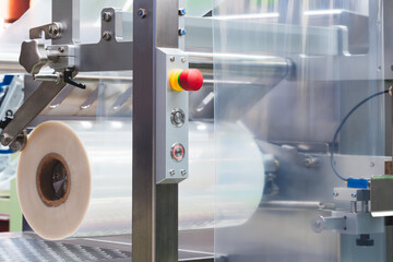 A machine with a roll of polyethylene plastic wrapping film on it. The machine is in a factory....