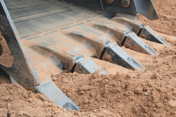 Excavator bucket with large teeth digs the ground close-up industrial concept background. © Aleksandr Matveev