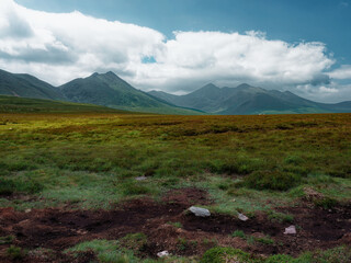 View of Mountain landscape across a verdant grassy field under a blue sky with fluffy clouds in County Kerry, Ireland.