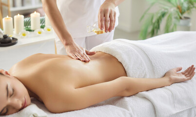 Therapist applies oil for a back massage to woman patient in spa salon, treatment therapy,...