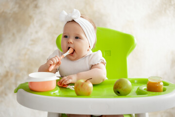 a toddler or a small child in a high chair eats fruit puree with a spoon