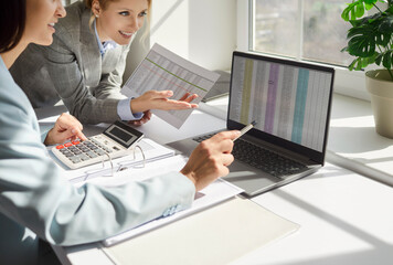 Concentrated businesswomen, female traders looking at laptop screen with stock market data, using...