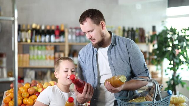 Father with boy hold packages plastic bottle and choose consider fruit juice in store. Market visitors choose make choice and view bottle juice. Client hesitates before buying, chooses drink
