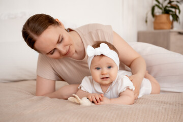 mom and baby, mother plays and admires her baby at home on the bed, mother gently hugs her baby,...