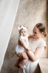 mom and baby, mother gently hugs her baby sitting at home on the window, maternal love and care