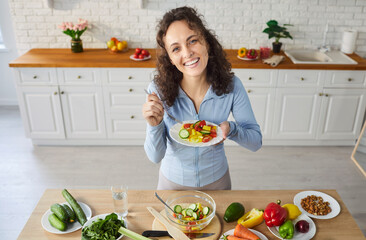 Portrait of a happy cheerful young woman holding plate with fresh healthy vegetable salad and...