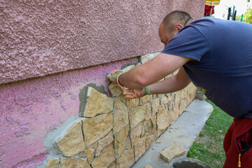 A worker in protective gloves carefully attaches decorative stone to the building's plinth.