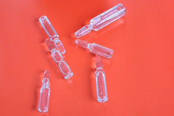 Transparent glass ampoules containing liquid are randomly scattered on a rich red background. The...