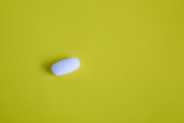 A single white oval pill rests on a vibrant yellow background, creating a minimalist and clean...