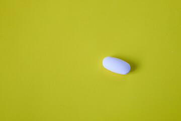 A rich yellow background serves as a vibrant canvas for a single white oval pill, elegantly...