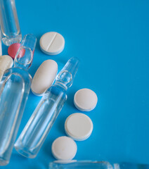 A close-up of clear ampoules and white pills with one pink tablet, scattered on a vibrant blue...