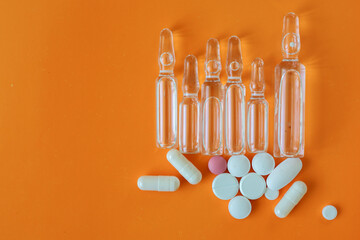 A set of clear glass ampoules and colorful pills arranged on a vibrant orange background. This...