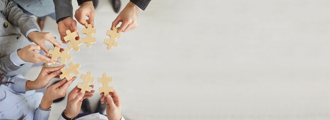 Group of business people standing in circle and holding wooden jigsaw puzzle. Top view of hands of company employees stacking pieces during teamwork activity. Unity and collaboration concept. Banner.